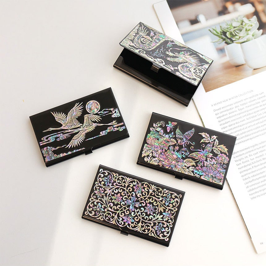 Decorative black name card holders with floral and bird designs on a white surface.